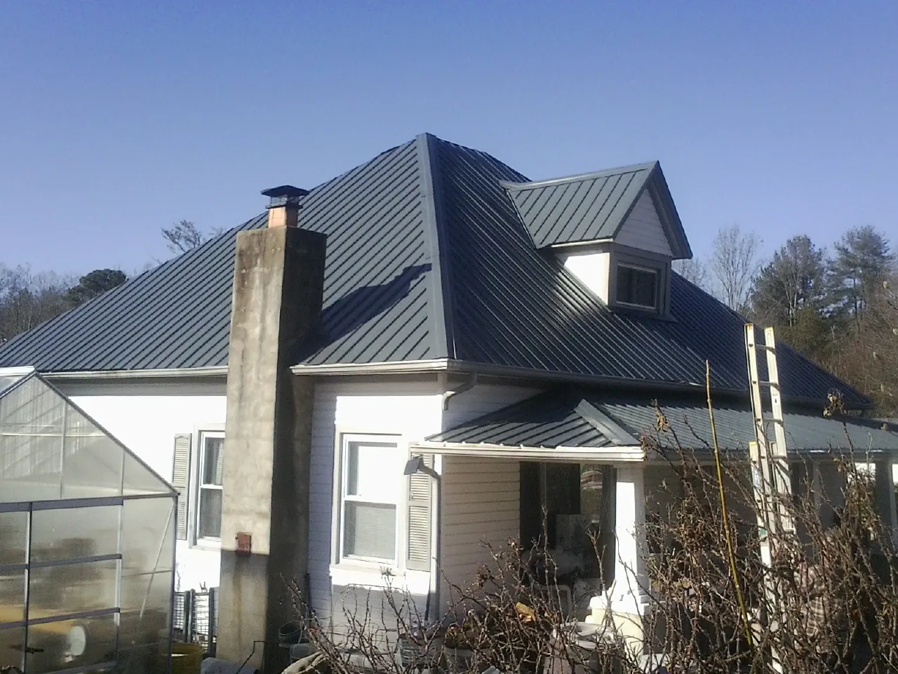 Dark blue standing seam metal roof on a white farmhouse with dormer — Slate & Tile Roof Repair by Roofing Brothers in Table Grove