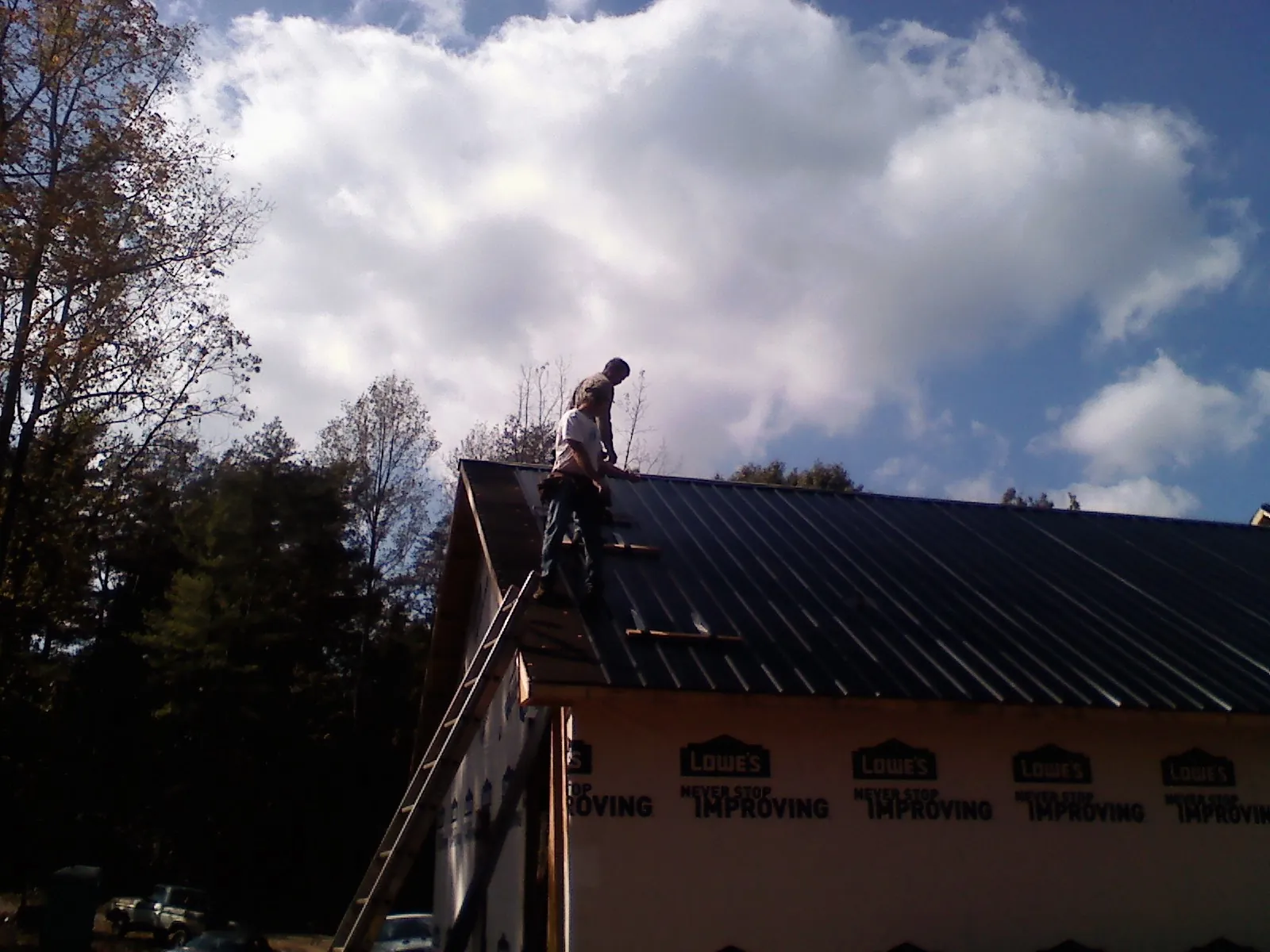 Roofer fastening dark metal panels high against a cloudy sky, from a Roof Inspection job in Table Grove