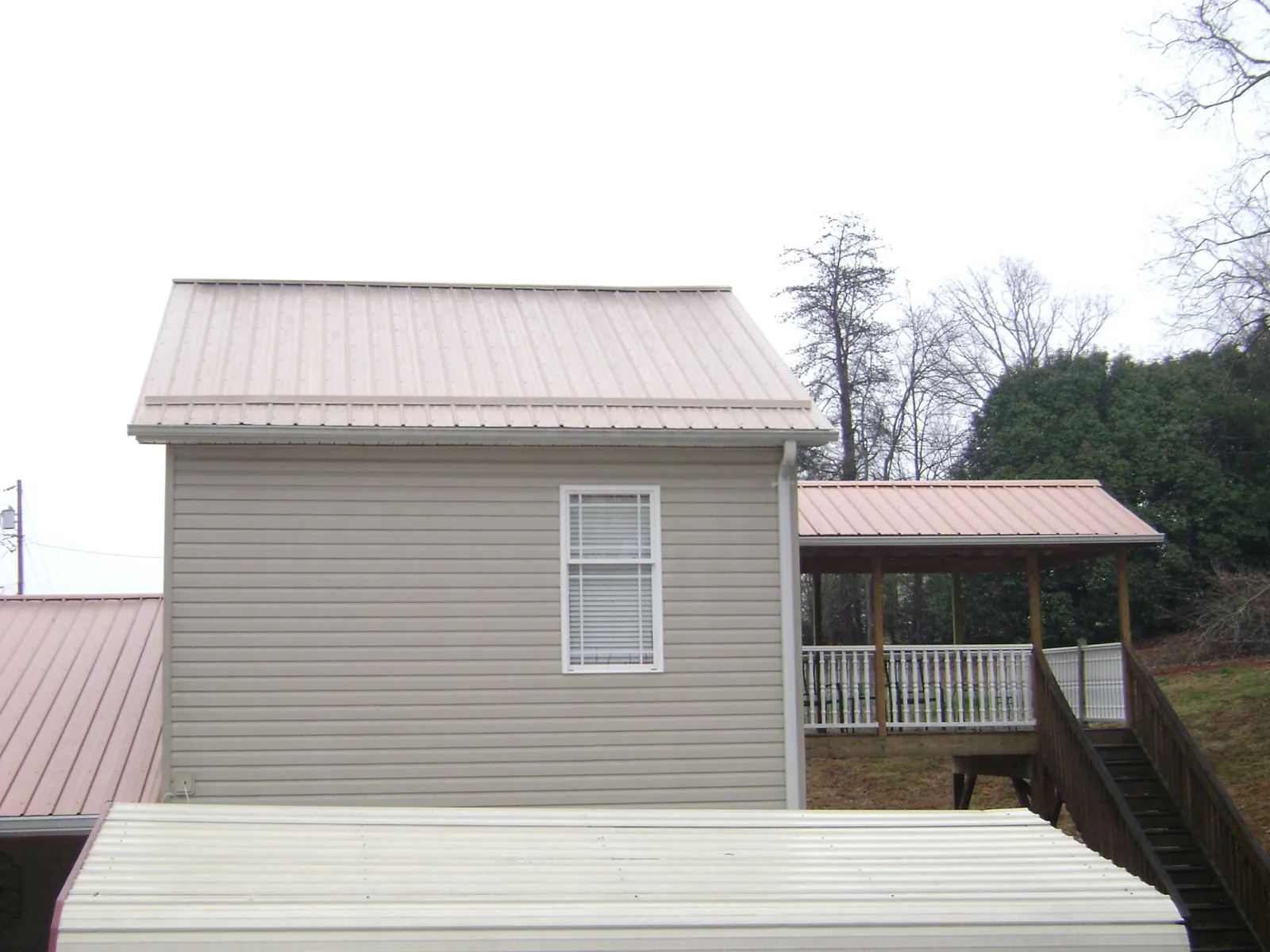 Tan metal roofs on a two story addition and attached porch, from a Roof Replacement job in Table Grove